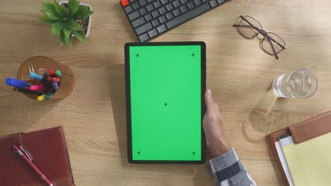 vista de arriba hacia abajo de una computadora portátil con pantalla verde simulada pantalla chromakey en un escritorio de oficina de madera al lado de la libreta con bolígrafos, gafas y un vaso de agua.