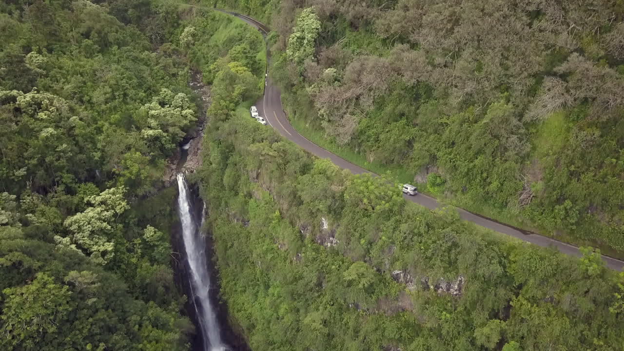 Slowly rising above a deep hidden jungle waterfall below the winding narrow Hana Hwy, aerial