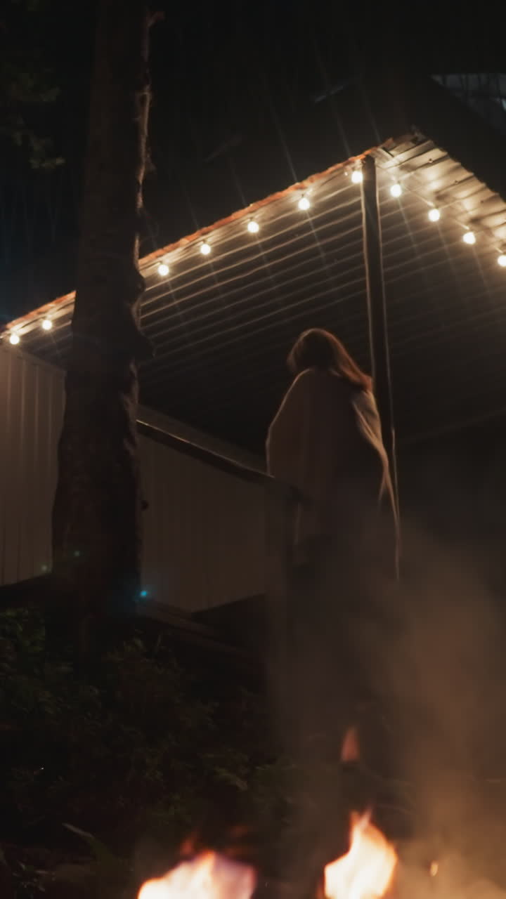 마당에서 계단을 오르는 여자 - 은 숲 사이에서 관광객을위한 시골 집의 사적인 영토의 야간 풍경 - 밤에는 캠프에서 불꽃과 함께 산책합니다.