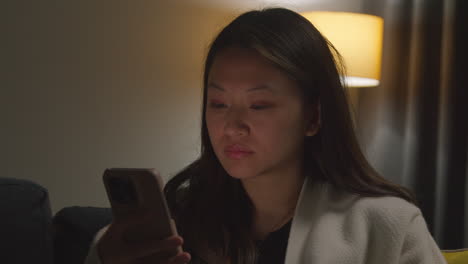 close up of woman spending evening at home sitting on sofa with mobile phone scrolling through internet or social media 1