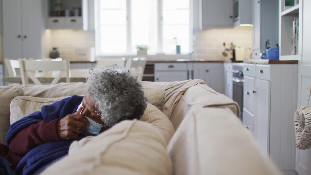 Sick senior african american woman covered with blanket sneezing while lying on the couch at home
