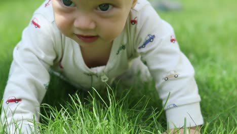 funny baby child lying on green grass garden, making face, smiling, exploring