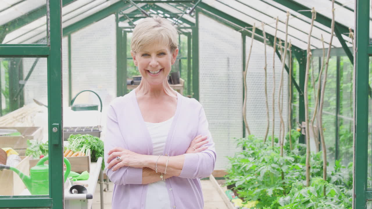 온실 의 문 에 서서 채소 를 재배 하는 고위 여성 의 초상화 와 팔 을 접는 것