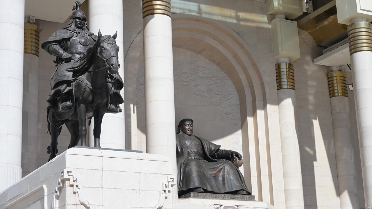 Una giornata di sole a Piazza Sukhbaatar, Ulaanbaatar, mette in risalto l'imponente statua in bronzo di Gengis Khan, affiancata da una statua di soldato a cavallo, di fronte al Palazzo del Governo.