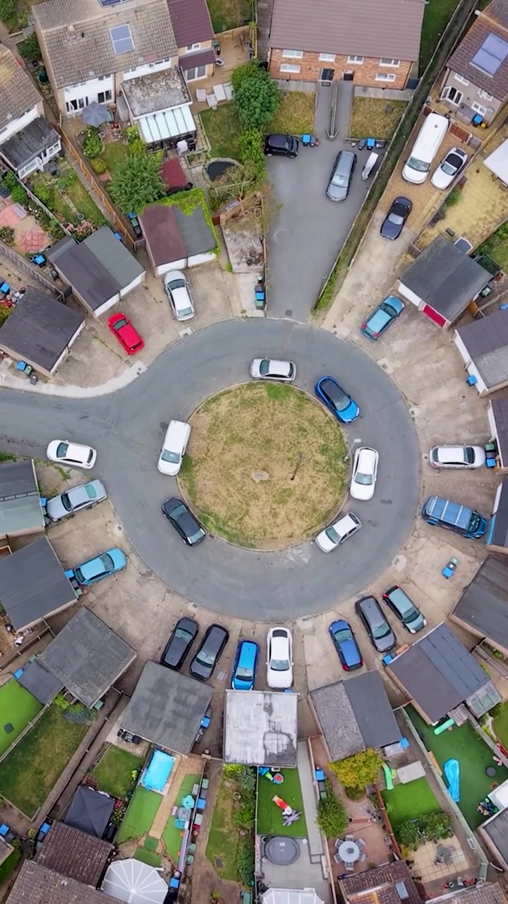 Roundhills, Waltham Abbey top-down vertical drone shot rotates over unusual circular cul-de-sac, parked cars and suburban houses with gardens, revealing neighborhood layout and urban planning.