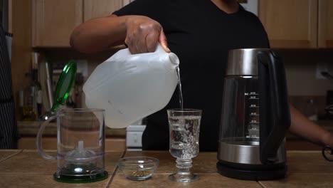 measuring distilled water into a glass to heat for a special cup of herbal, organic tea