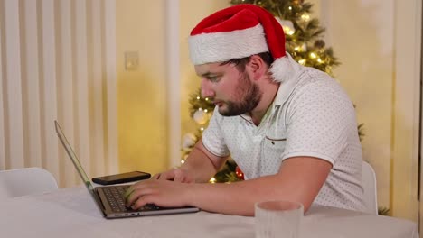 Kaukasischer-Unternehmer-Geschäftsmann,-Der-Von-Zu-Hause-Aus-Mit-Einer-Weihnachtsmütze-Während-Der-Weihnachtsferien-Arbeitet-Und-Auf-Einem-Laptop-Mit-Einem-Glas-Whisky-In-Der-Nähe-Eines-Weihnachtsbaums-Tippt