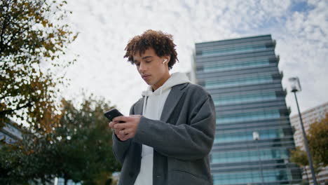 Lockiger-Teenager-Tippt-Smartphone-Auf-Der-Straße,-Nahaufnahme.-Junger-Mann-Hört-Musik