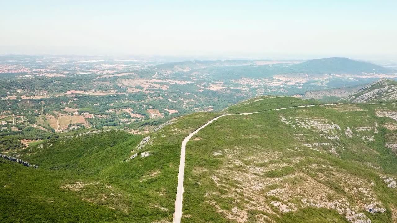 Breathtaking aerial view capturing a winding road meandering through the lush green slopes of the Arrábida mountain range, overlooking the scenic Setúbal Peninsula