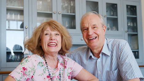 Retrato-De-Una-Pareja-Senior-Sonriente-Sentada-En-La-Mesa-De-La-Cocina