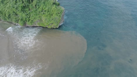 Top-down-aerial-drone-shot-over-polluted-sewage-water-and-floating-trash-with-debris-over-dead-coral-reef-mixing-with-turquoise-water-and-tropical-coastine-in-Bali-Indonesia