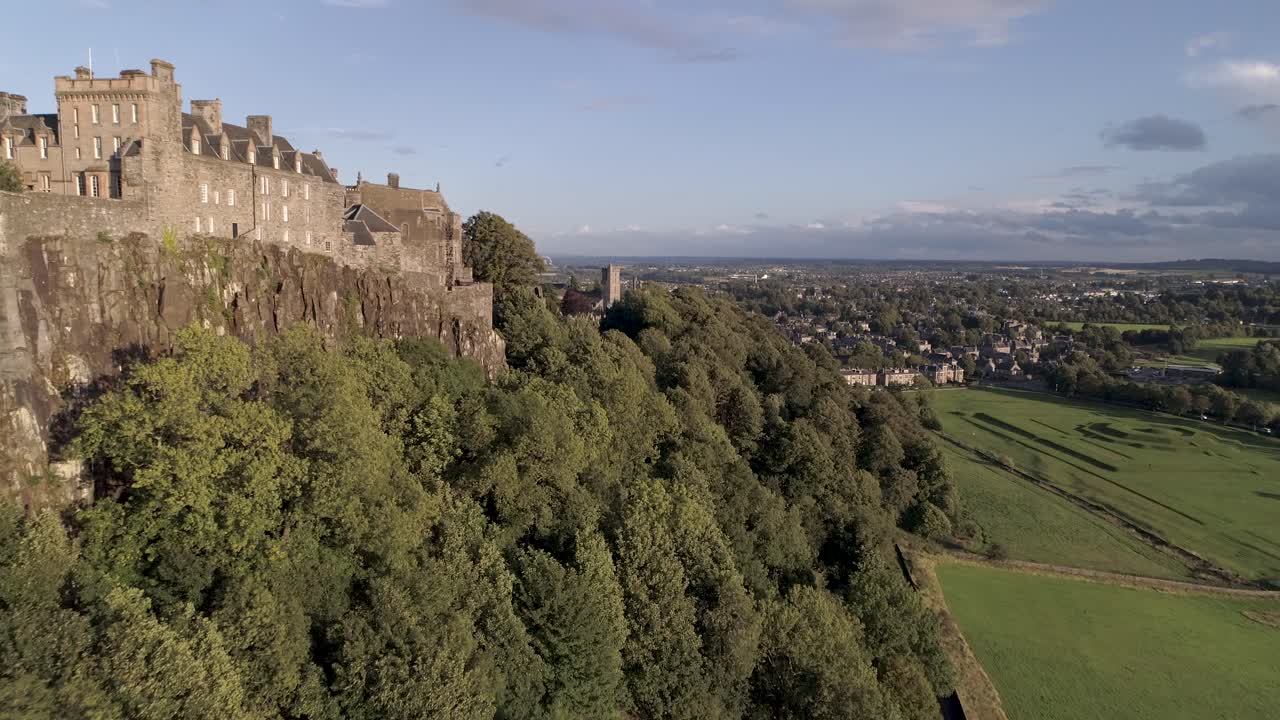 Ripresa aerea in volo verso est lungo i bastioni del Castello di Stirling in una giornata limpida e soleggiata, che rivela la chiesa e il cimitero