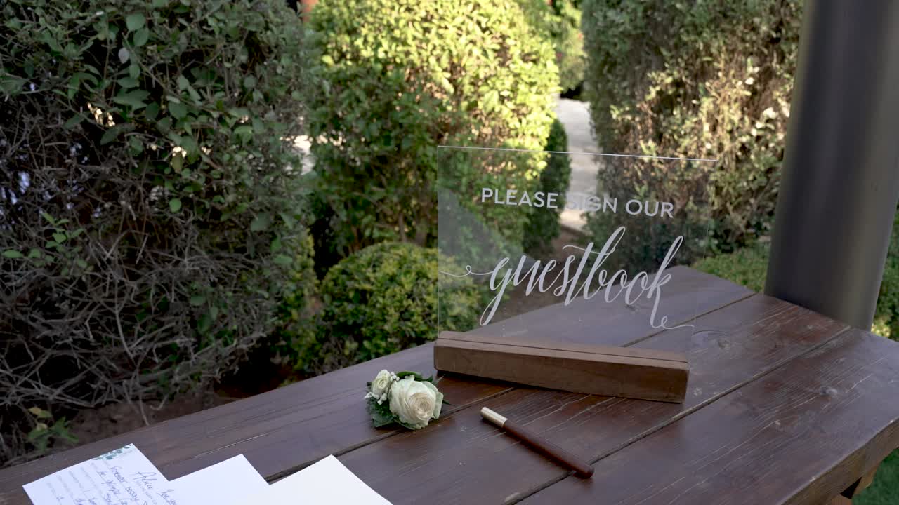 In a serene garden setting, guests gather to sign the guestbook, creating lasting memories at a beautiful outdoor wedding filled with love and joy