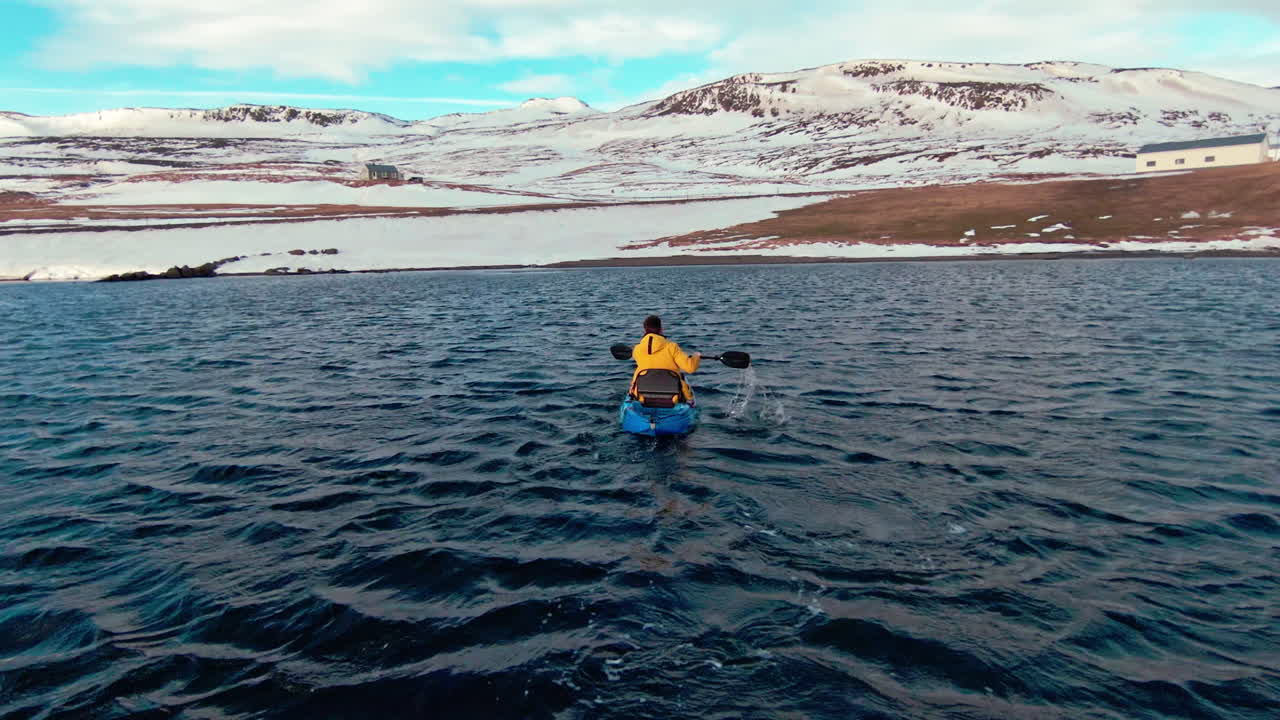 노란색 재 ⁇ 을 입은 남자가 카야크, 야생 바다 파도에서 해안에 도착하려고합니다.