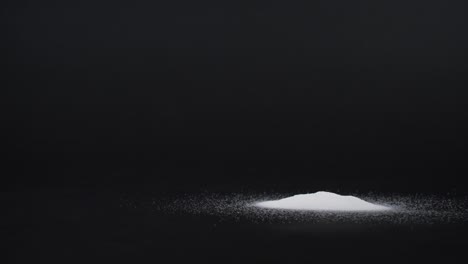 pouring-two-different-amounts-of-white-powder-against-black-background