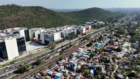 panoramic aerial view of a sprawling modern it park and new residential high-rises in chennai, alongside a busy highway and railway, with lush hills in the background.