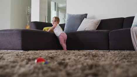 cute caucasian baby standing while holding the couch at home