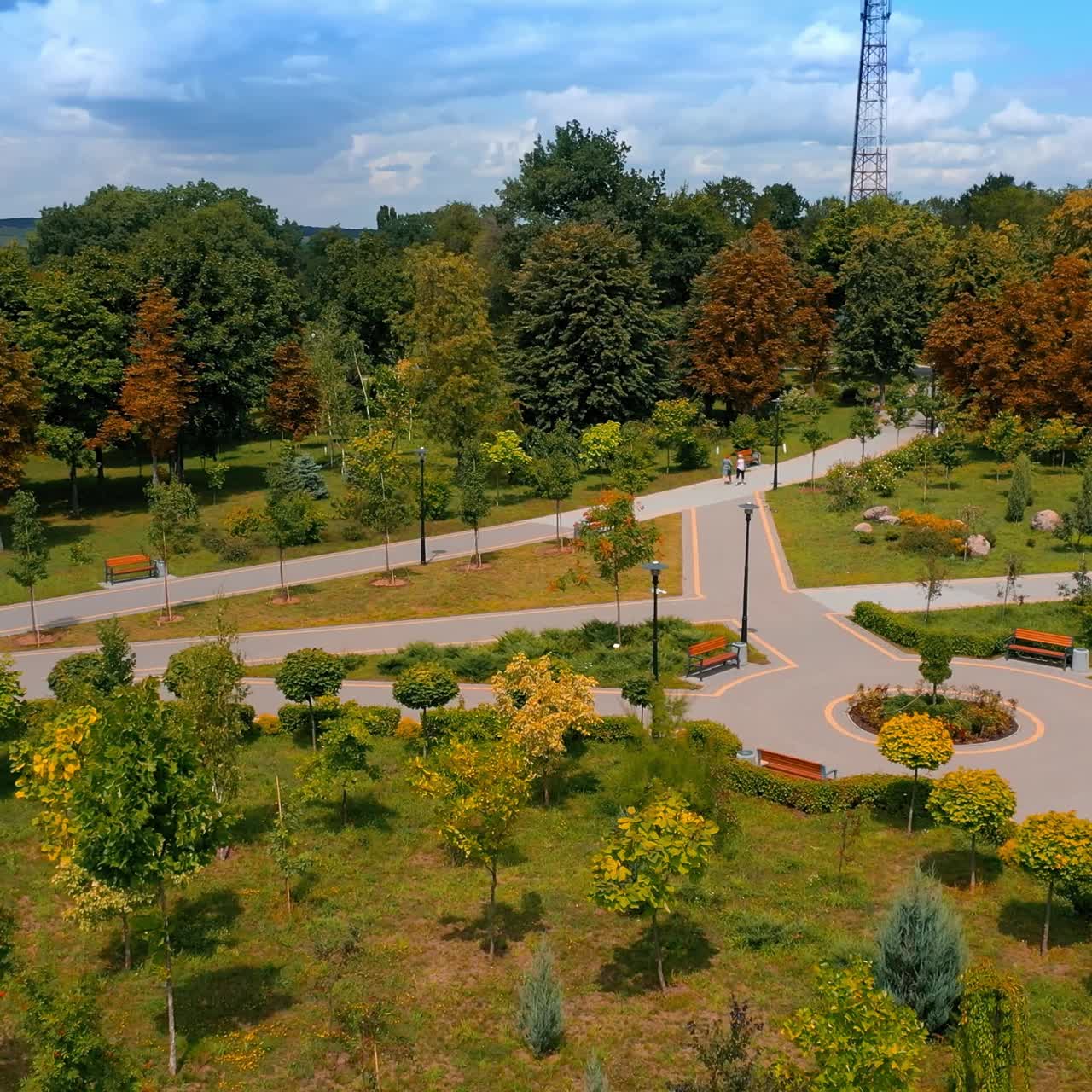 Well-kept green park with green trees on sunny clear day. City garden with neat paths and flower-beds from aerial view