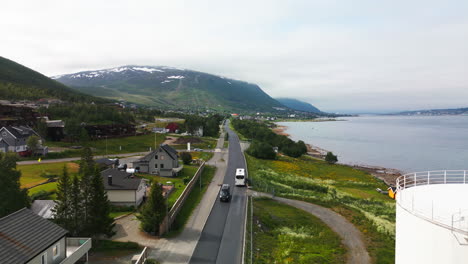 Drone-tracking-shot-of-white-bus-on-scenic-road-next-to-fjord,-Tromso,-Norway