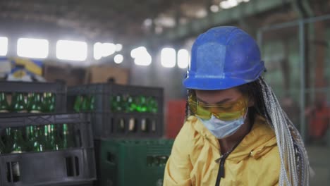 woman worker in mask controls the recycle waste separation of recyclable waste plants. sorting glass bottles into boxes for further disposal. slow motion