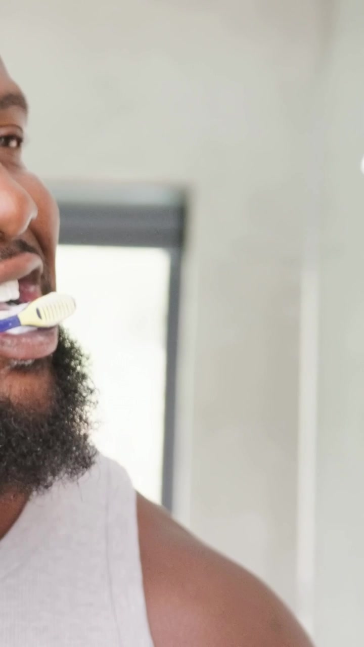 Starting routine, bearded man in gray-tank brushing teeth in home bath with brush, foam, copy space