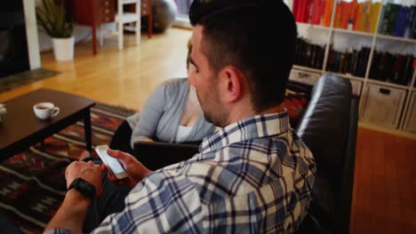 Una-Mujer-Usando-Una-Computadora-Portátil-Mientras-Un-Hombre-Usa-Un-Teléfono-Móvil-Y-Un-Reloj-Inteligente-En-La-Sala-De-Estar