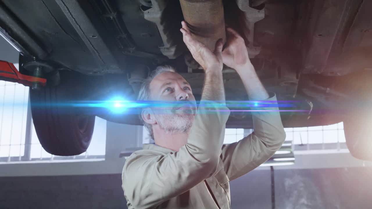 Senior mechanic inspecting exhaust pipe on lift in automotive garage, showing lens flare overlay
