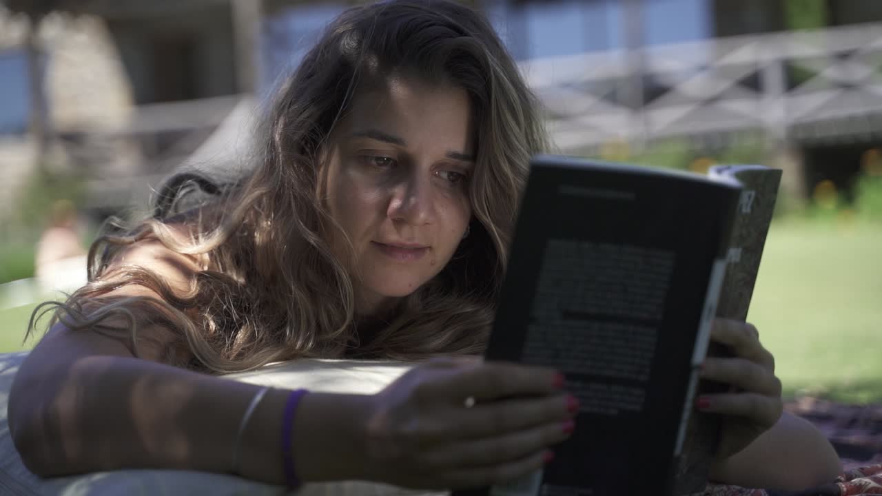 joven latina interesada en estudiar leer libros al aire libre en el césped con vegetación y fondo de casa a cámara lenta 60 fps