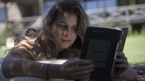 young latin female interested studying reading book outdoors on the grass with a vegetation and house background slow motion 60 fps