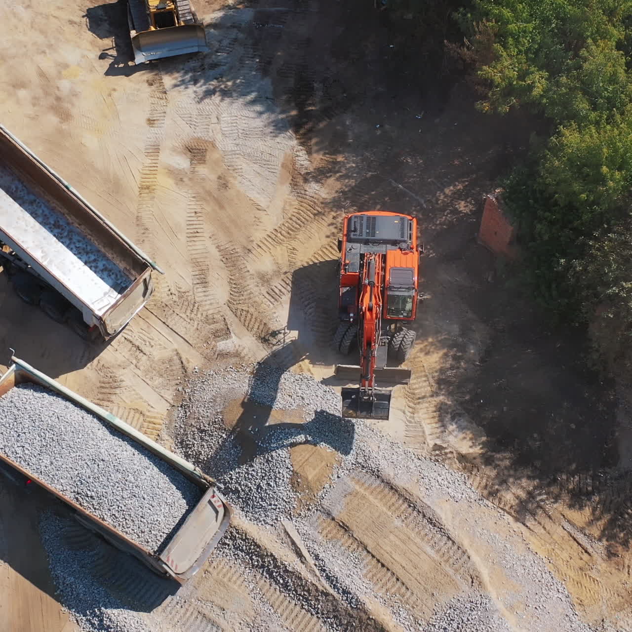 View from above on excavator and two trucks. Excavator working near the machinery with granite stones. Aerial view.