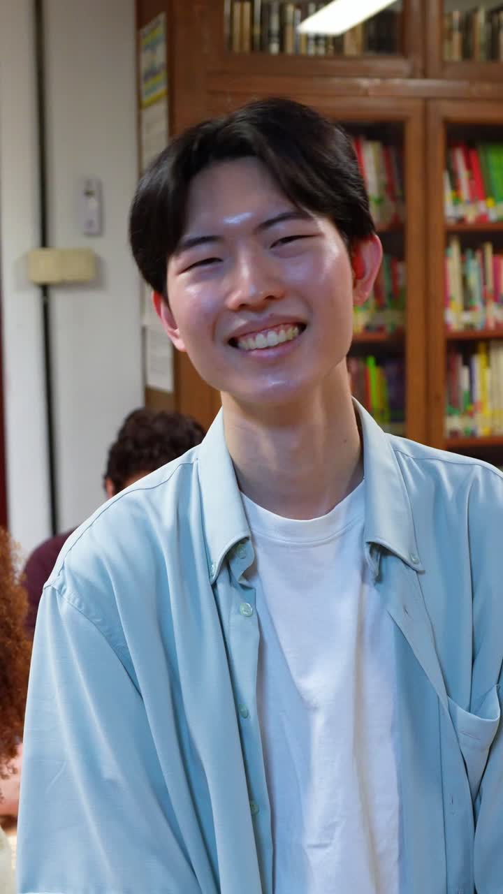 Giovane uomo asiatico felice che sorride in una biblioteca