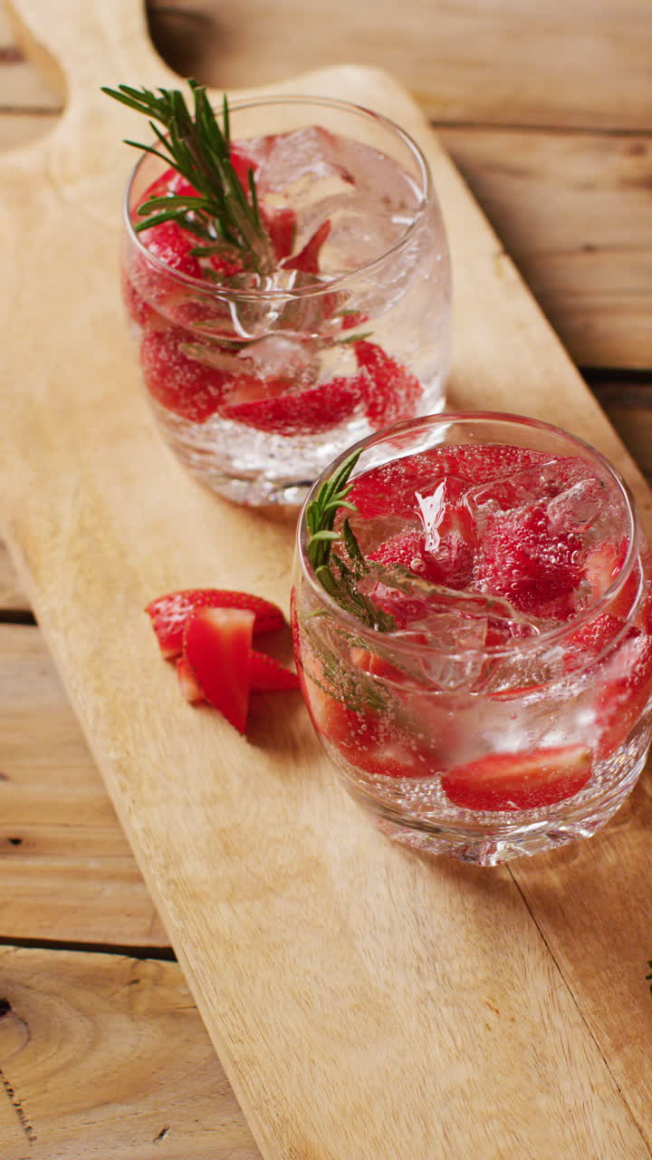 Vertical video of close up of drinks with strawberries on wooden board, with copy space