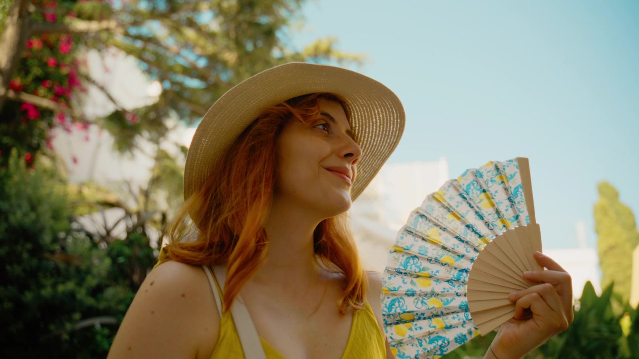 Una donna usa un ventaglio e sorride in un giardino sull'isola di Capri.