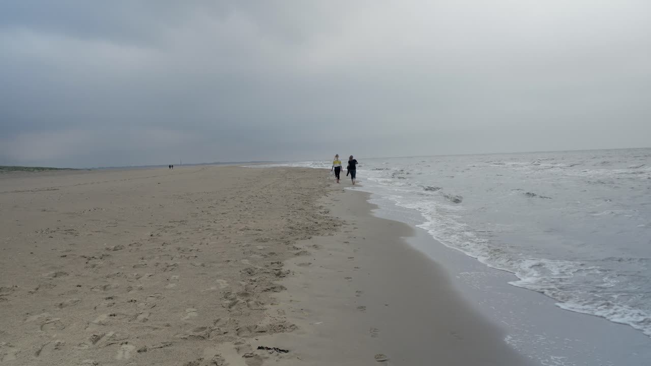 텍셀 섬에서 흐린 날 북해 해안을 따라 걷는 두 여자 친구