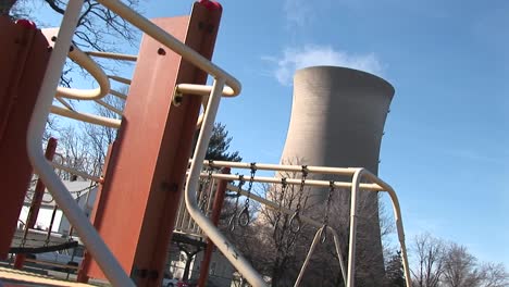 Se-Utiliza-Equipo-De-Juegos-Para-Niños,-Mientras-Que-Una-Central-Nuclear-Se-Muestra-En-El-Fondo.