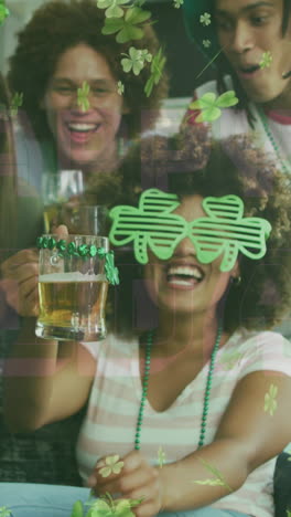 animation of clovers over happy diverse friends wearing clover shape items and drinking beer