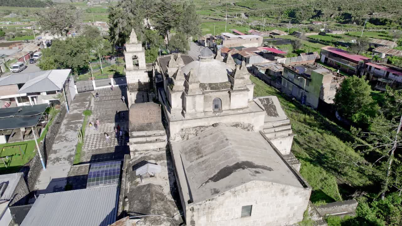 Aerial shot flying behind the Church of Chiguata, revealing the plaza and the majestic towers of the church in a smooth pan.