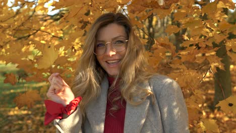 Blonde-Frau-Lächelt-Und-Spielt-Mit-Gelben-Und-Goldenen-Blättern-Im-Herbstpark