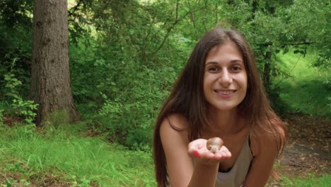 una mujer en una caminata en un bosque verde sosteniendo un caracol y lanzándole un beso a la cámara