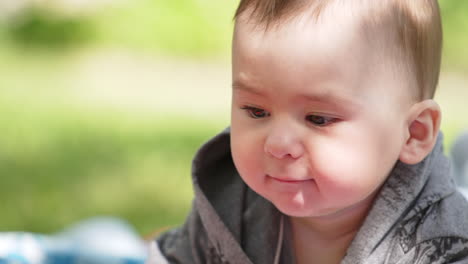 adorable active baby boy wearing grey shirt lies in nature. funny boy waving hands and feet. close up. blurred backdrop.