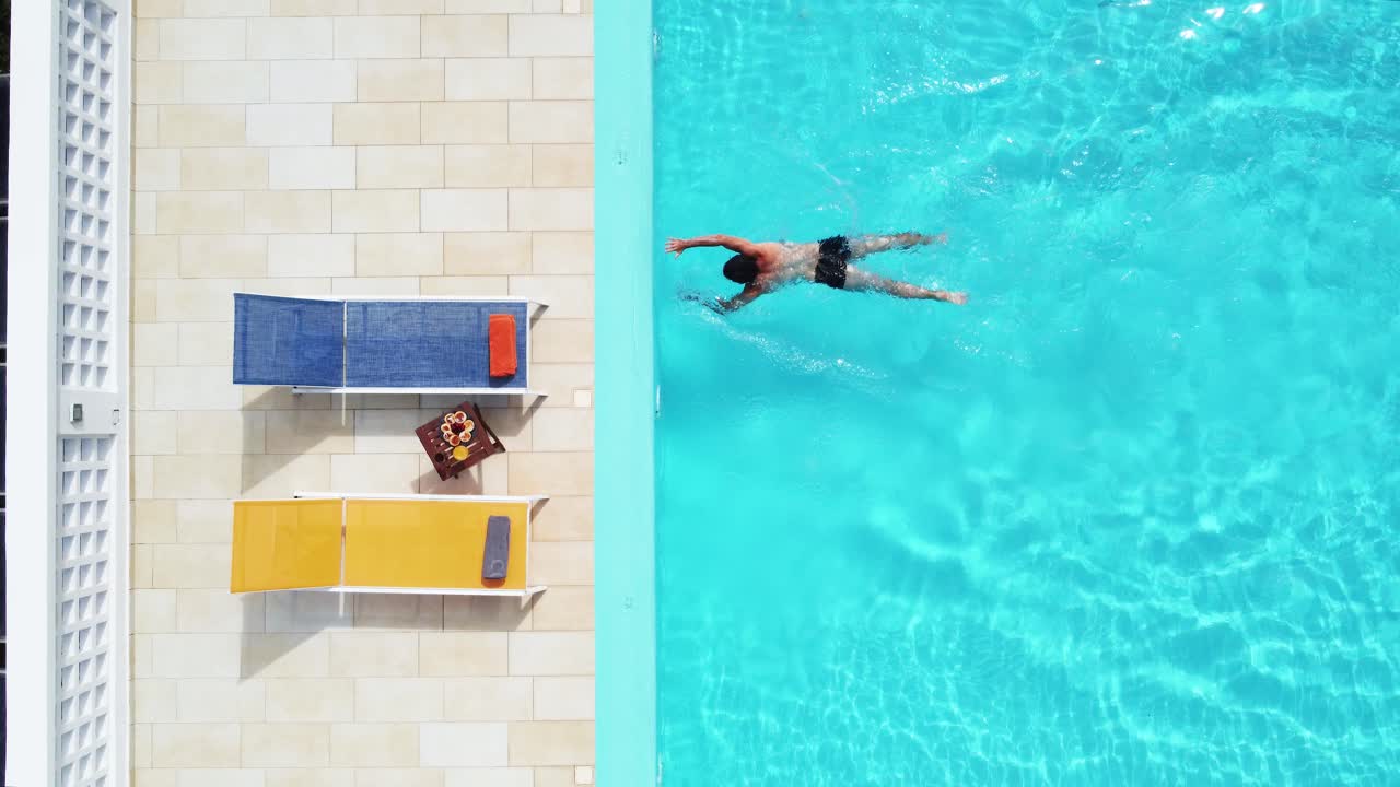 Draufsicht auf einen Mann, der in einem Resort-Pool schwimmt, Sommerurlaub, Sonnenliegen.