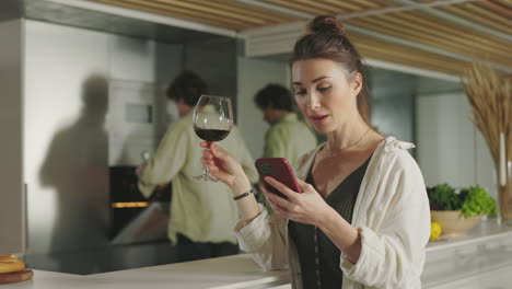 woman enjoys wine and phone in a modern kitchen with a partner
