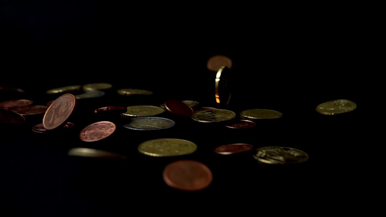 Coins fall on a black background. Slow motion