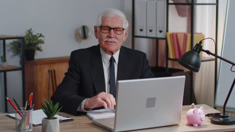 Senior-business-man-waves-hand-palm-in-hi-gesture-greeting-welcomes-someone-webinar-at-home-office