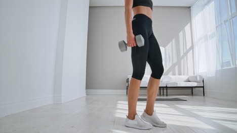 mujer joven en forma y enérgica haciendo ejercicios deportivos y de acondicionamiento físico con pesas para un estilo de vida saludable en la sala de estar en casa durante un día soleado