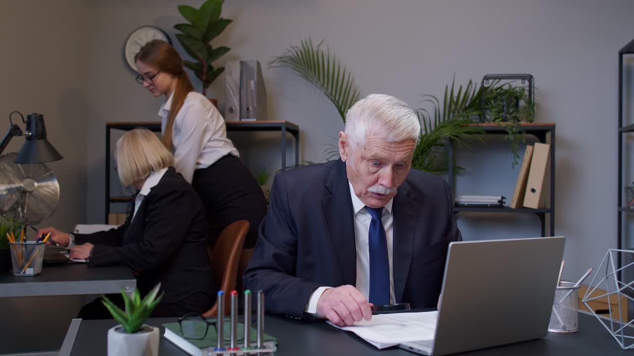 Ældre mandlig revisor læser dokumenter, analyserer finansielle papirer og hæver hænderne i overraskelse.