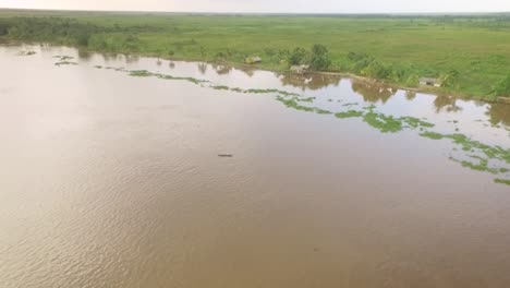 vista de drones de una pequeña canoa indígena que navega por el río orinoco con casas indígenas en la orilla