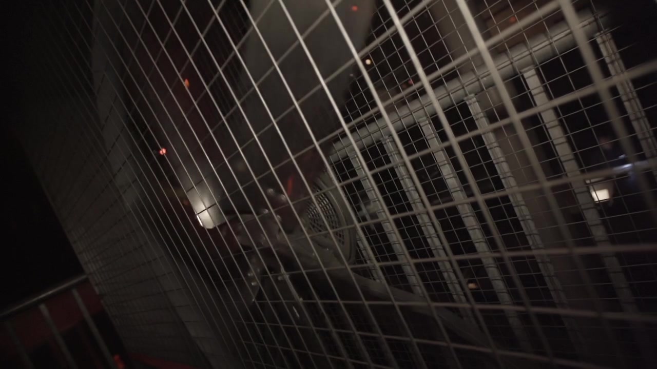 Slowmotion shot of a giant Nightclub Ventilator in a cage in the dark behind a grill or fence LOG