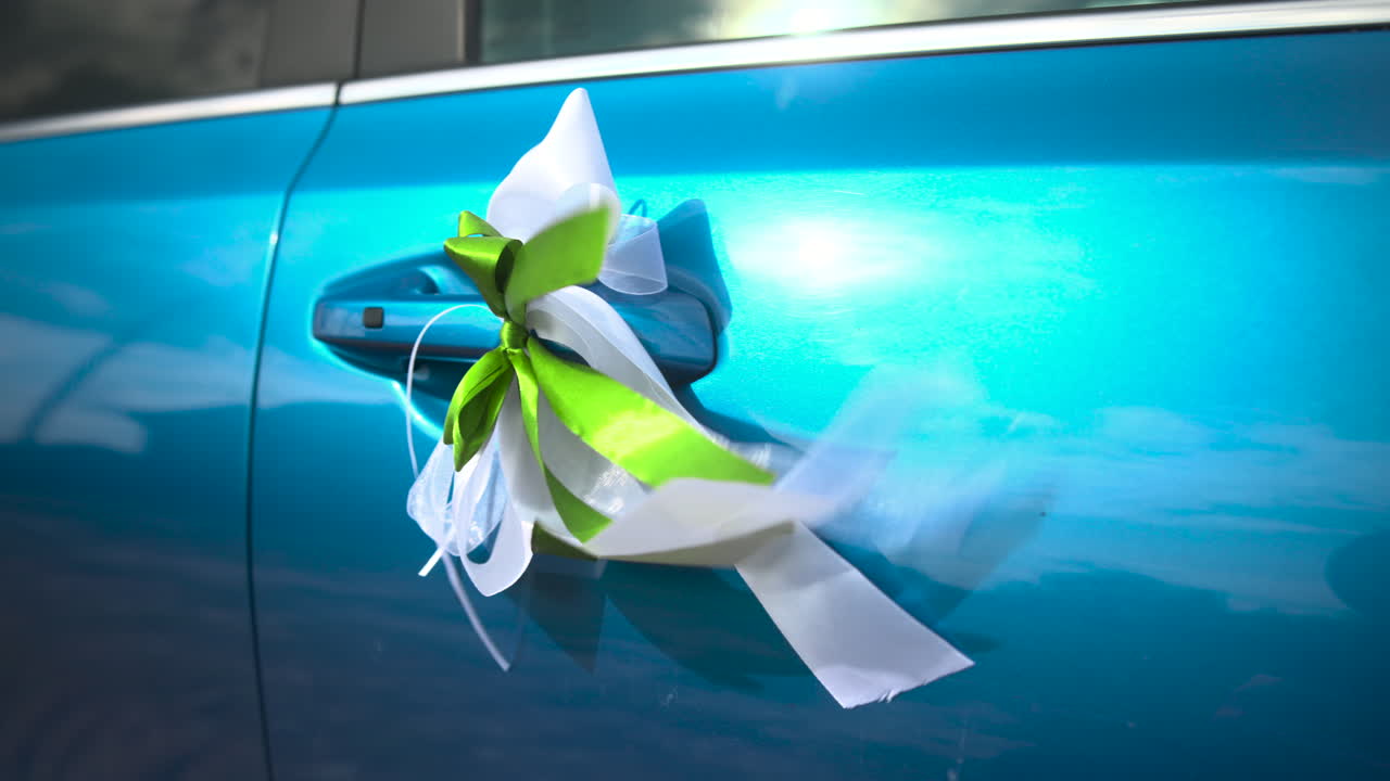 Heldere turquoise autodeurgreep versierd met wit en limoengroen lint, linten wapperen in de wind, close-up glanzend.