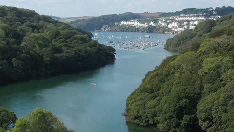 low aerial view pushing down the river fowey in cornwall, uk towards the coastal town of fowey with paddle boarders in frame